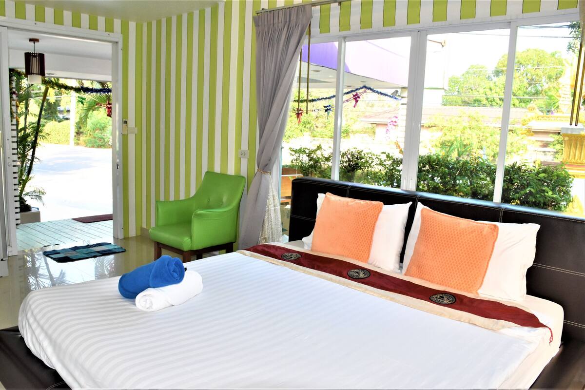 Habitación de hotel con una cama grande, una silla verde y vistas al exterior.