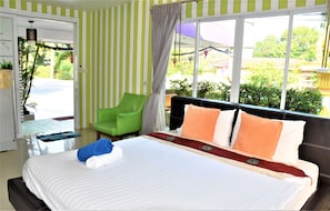 A hotel room with a large bed, a green chair, and a view of the outdoors. - Head Rock Home (Hua Hin)