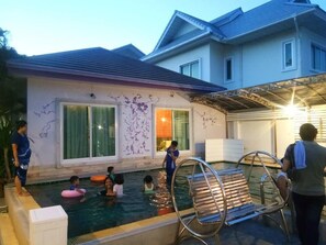 A swimming pool area with a house in the background, a covered patio, and a few people around the pool. - Head Rock Home (Hua Hin)
