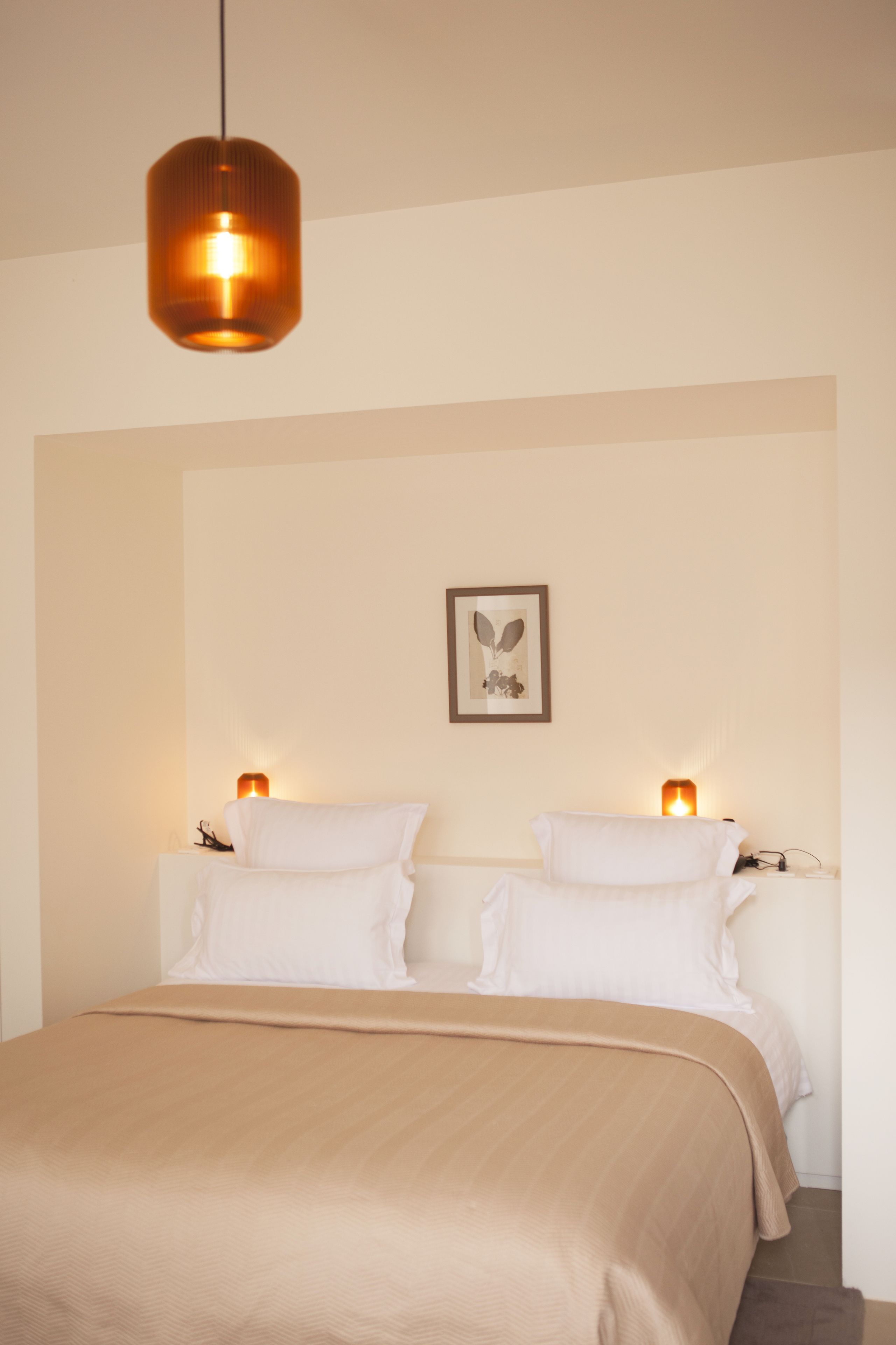 A neatly made bed with a beige bedspread, two bedside lamps, and a framed artwork on the wall.