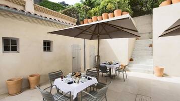 Un patio al aire libre con mesas y sillas, macetas de terracota y una escalera que lleva a un nivel superior.