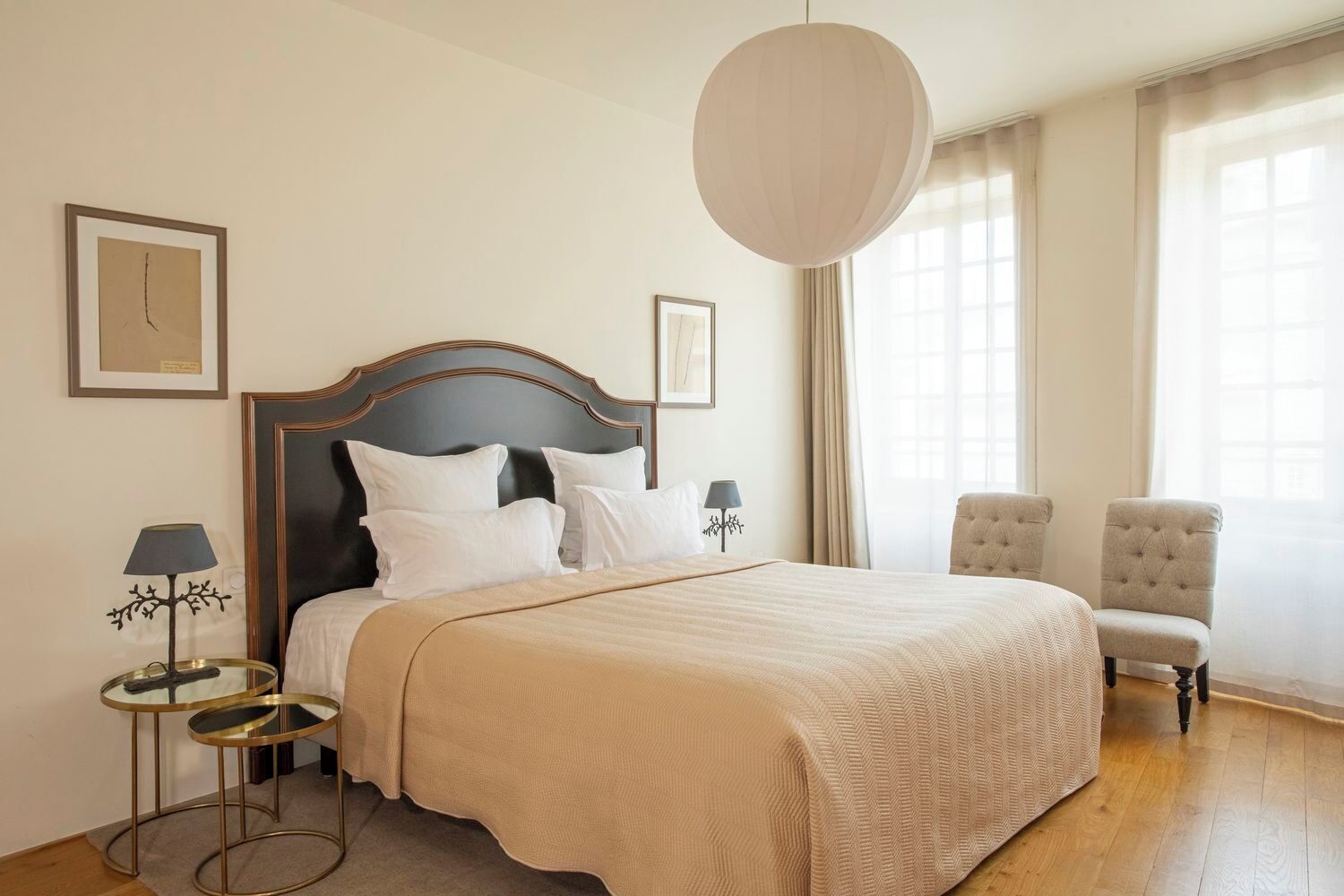Quarto de hotel com uma cama grande, duas mesas de cabeceira, uma cadeira e uma janela ampla com cortinas.