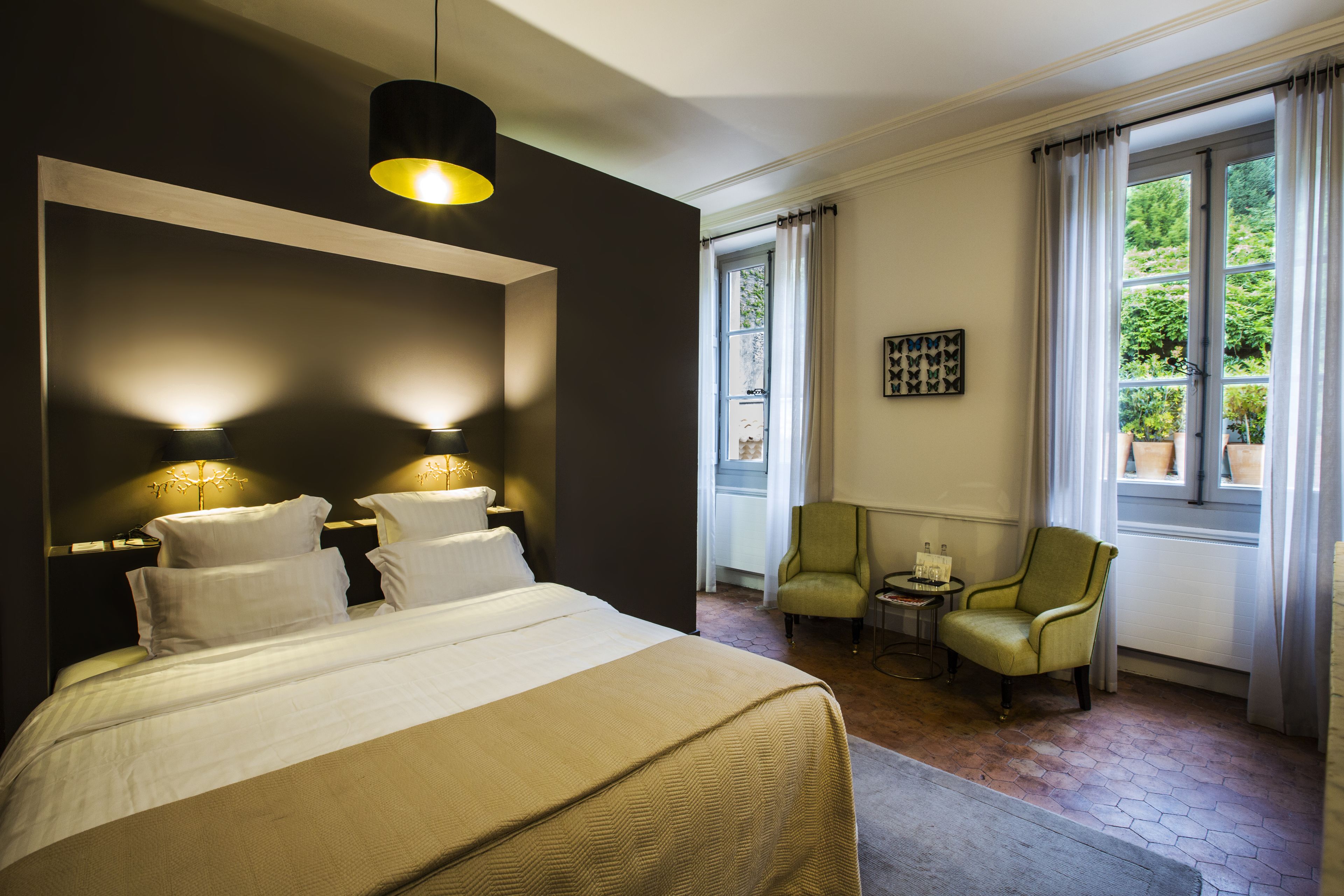 A hotel room with a large bed, two bedside lamps, a small table with a chair, and a window with curtains.