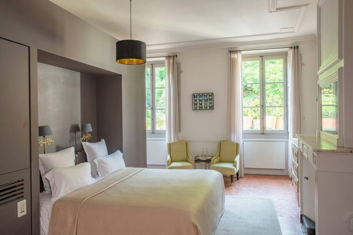 A hotel room with a large bed, two chairs, a small table, and a dresser.