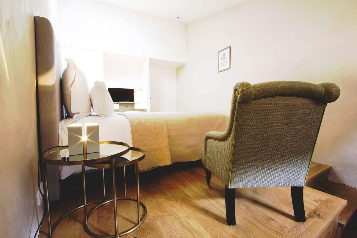 A hotel room with a bed, a chair, a small table, and a desk with a computer.