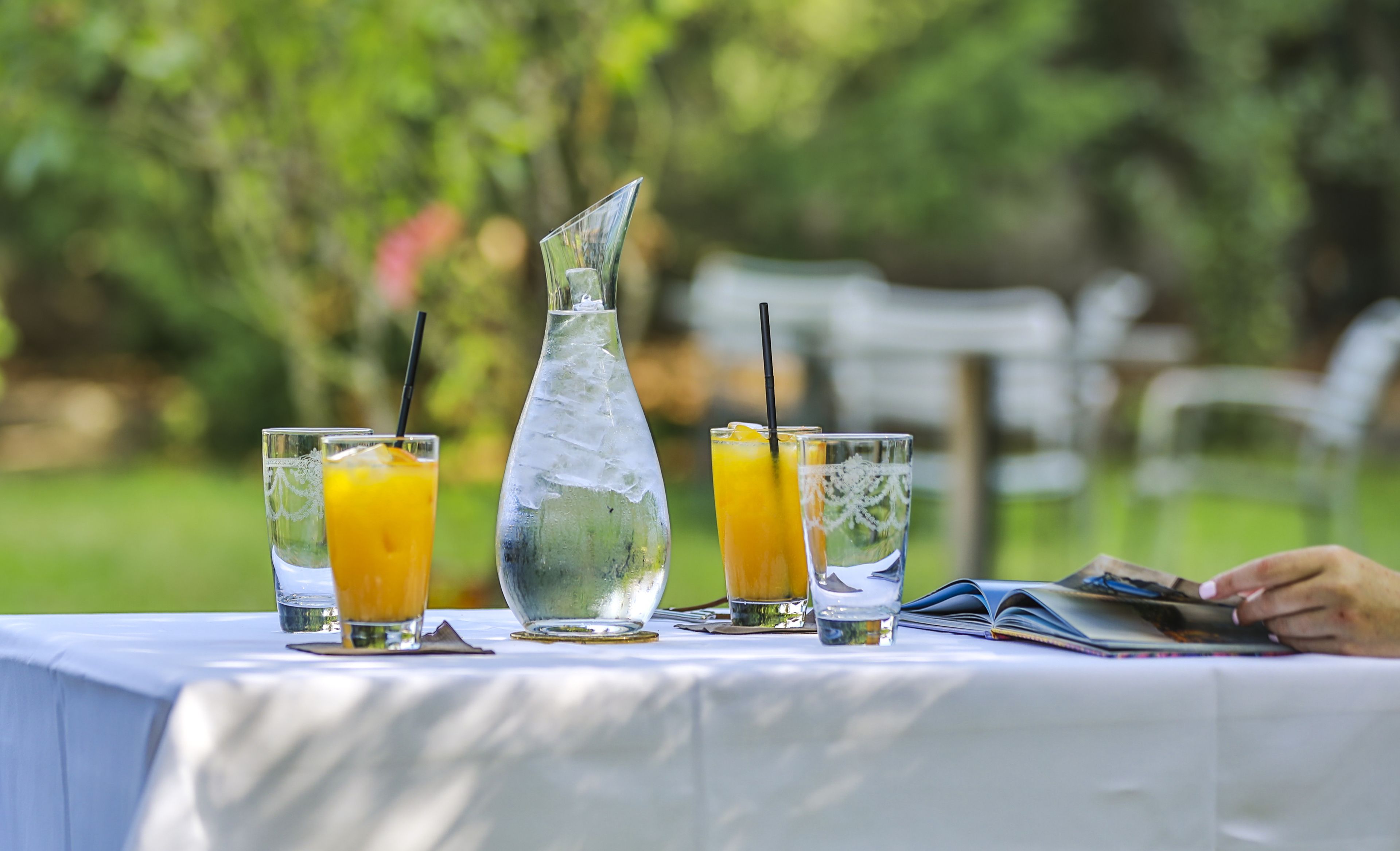 A table with a clear pitcher, two glasses of orange juice, and a book.