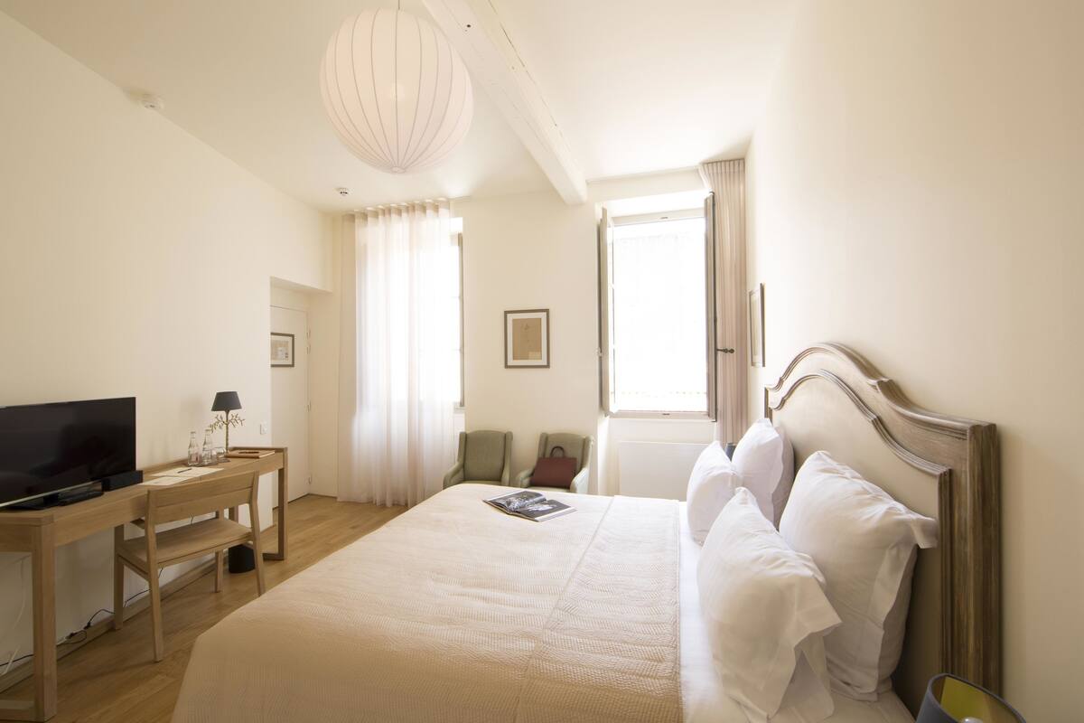 A hotel room with a bed, a desk with a television, a chair, and a window with curtains.