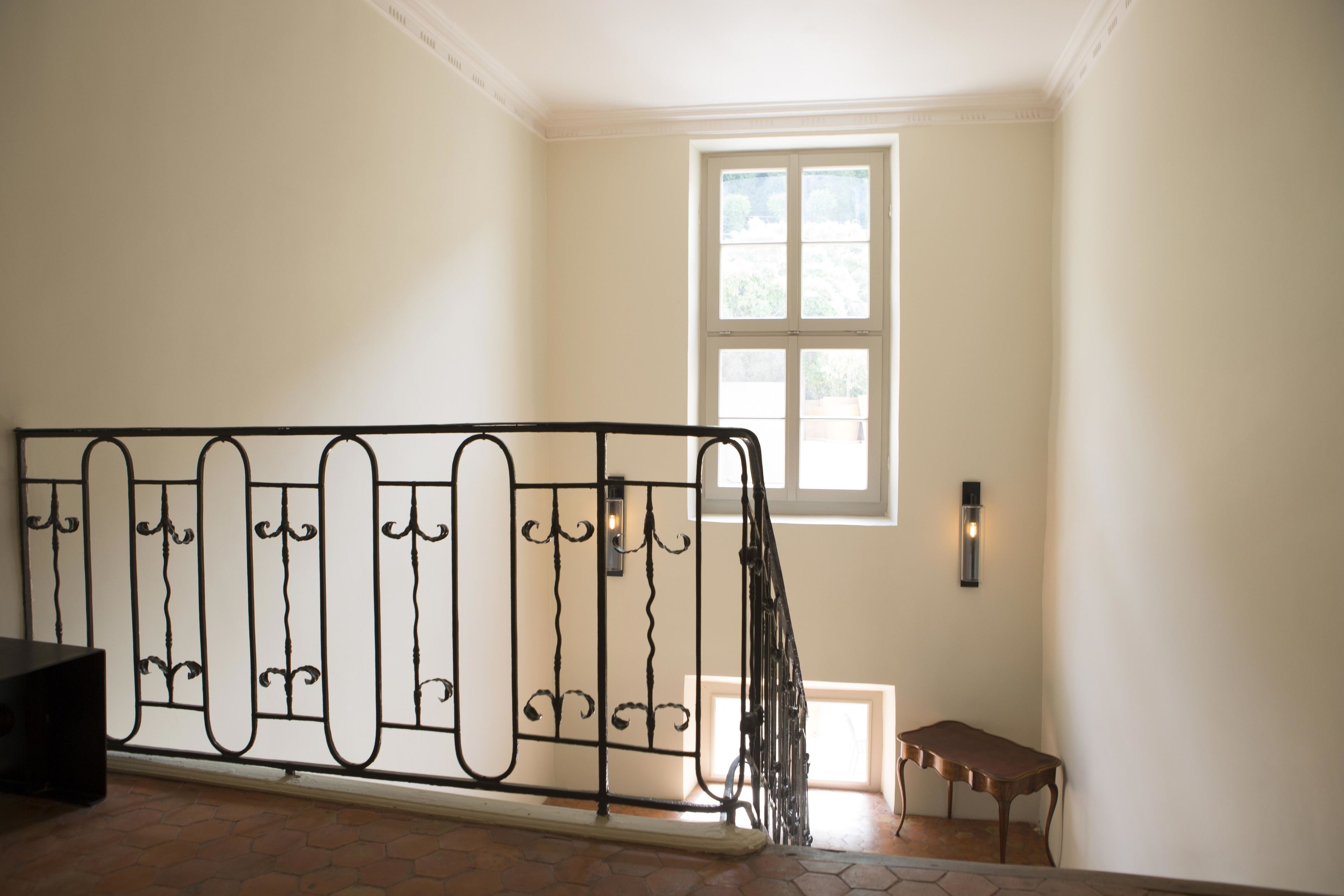 Una escalera con barandilla de metal negro, una mesita de madera y una ventana con luz natural.