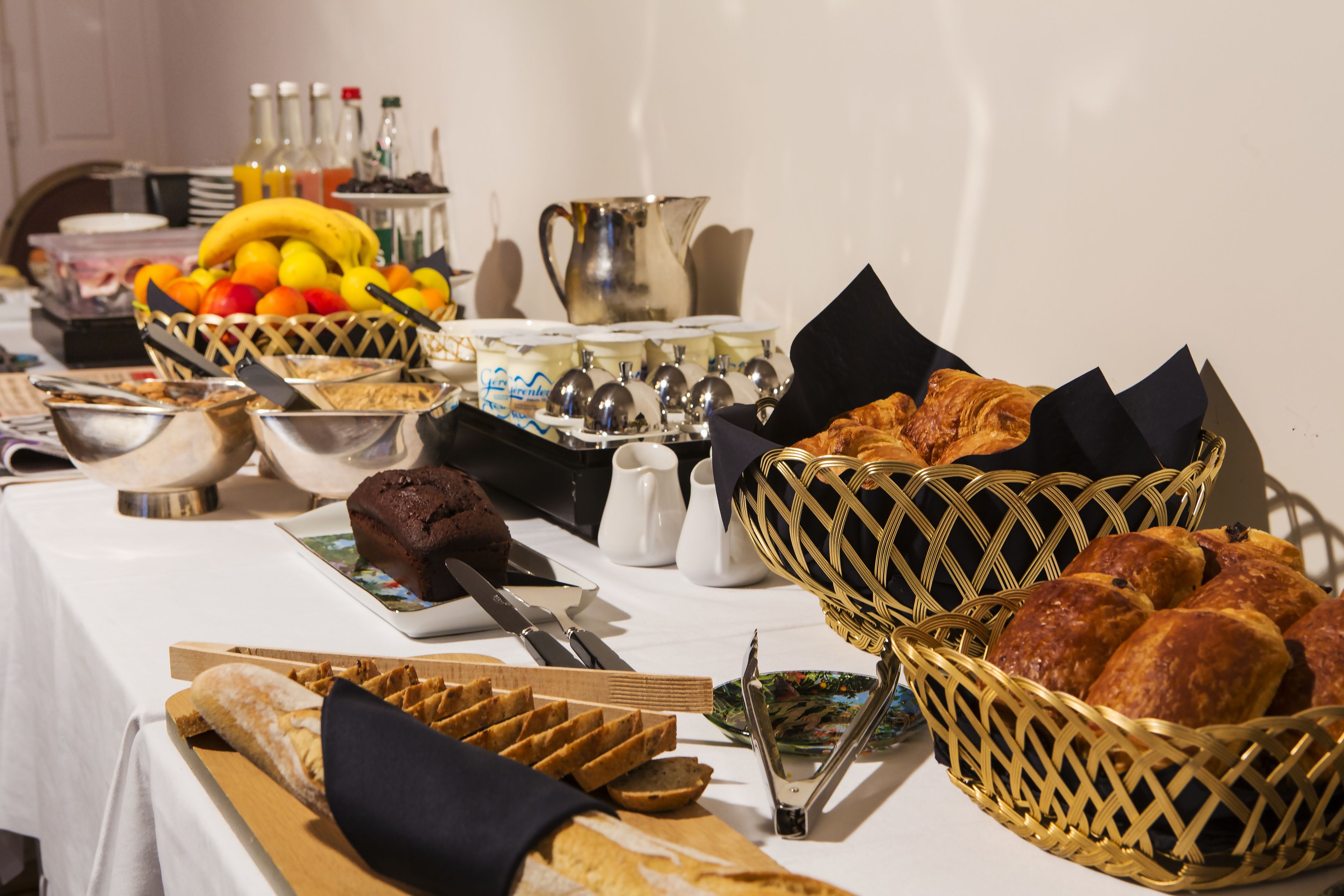 A buffet table with various food items including bread, pastries, and fruits.