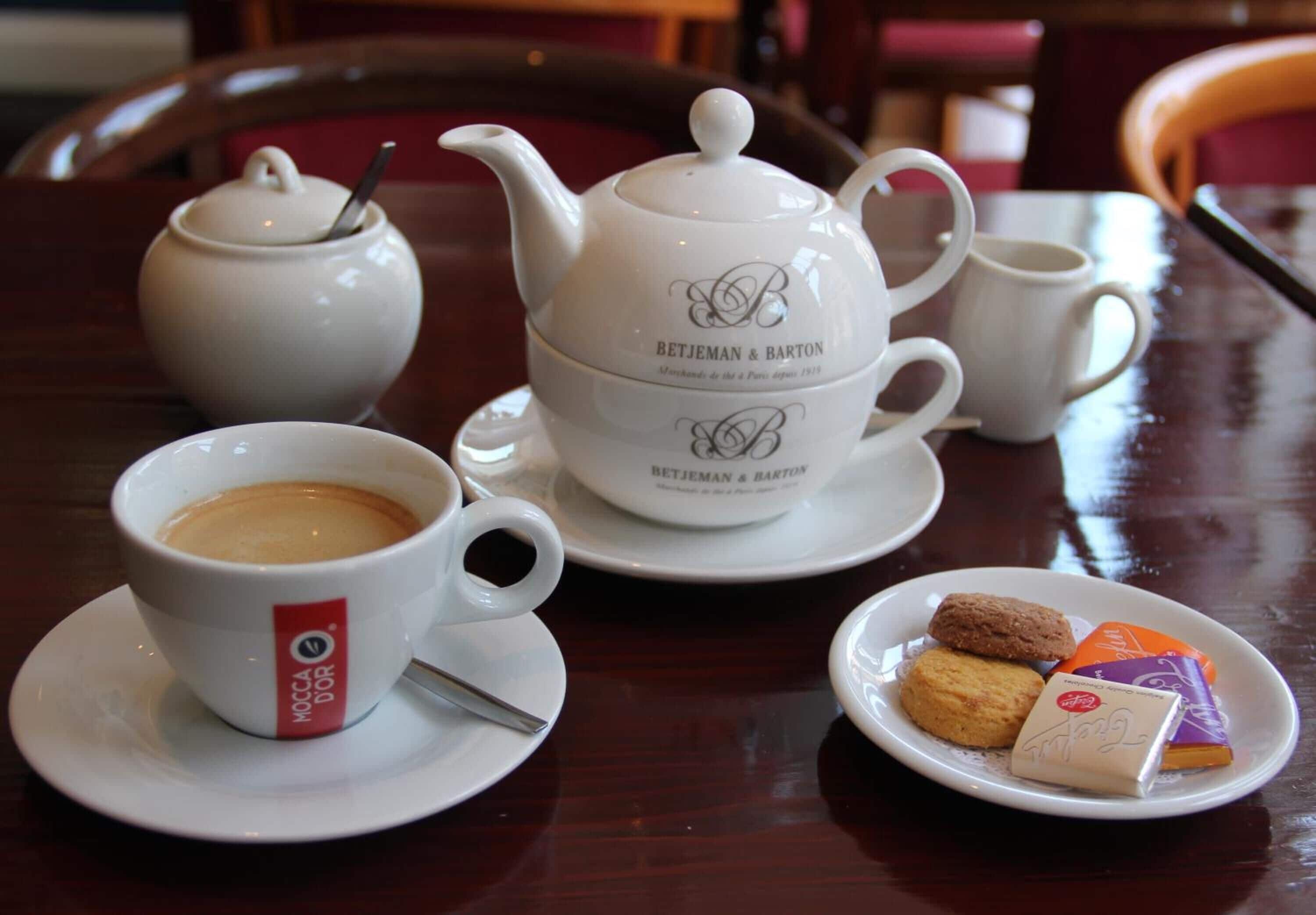 A table with a teapot, cups, and a plate of cookies.