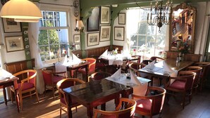 Um restaurante acolhedor com mesas de madeira e cadeiras vermelhas, quadros nas paredes e um lustre.