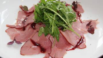 Un plato blanco con carne en lonchas finas y hojas verdes.