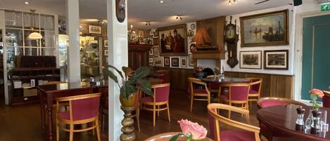 A dining area with wooden tables and chairs, a vase with a rose, and a clock on the wall.