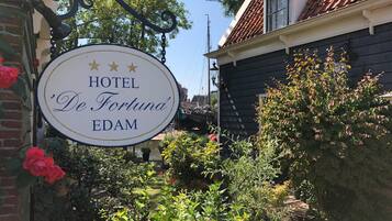 A sign for HOTEL 'De Fortuna' EDAM with a garden in the background.