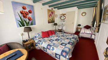 A bedroom with two beds, a sitting area with a chair, a small table, and a painting of tulips on the wall.
