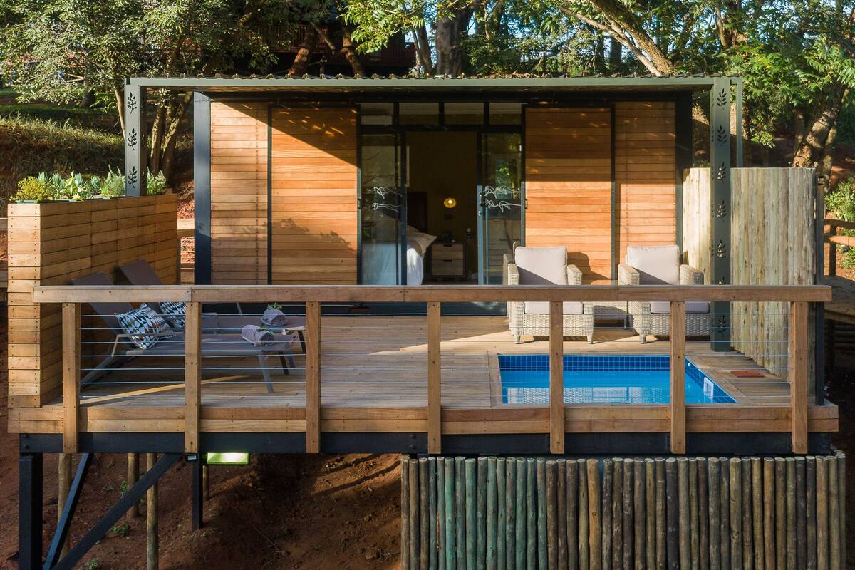 A modern wooden deck with a pool, a bedroom with a large window, and a dining area with outdoor furniture.