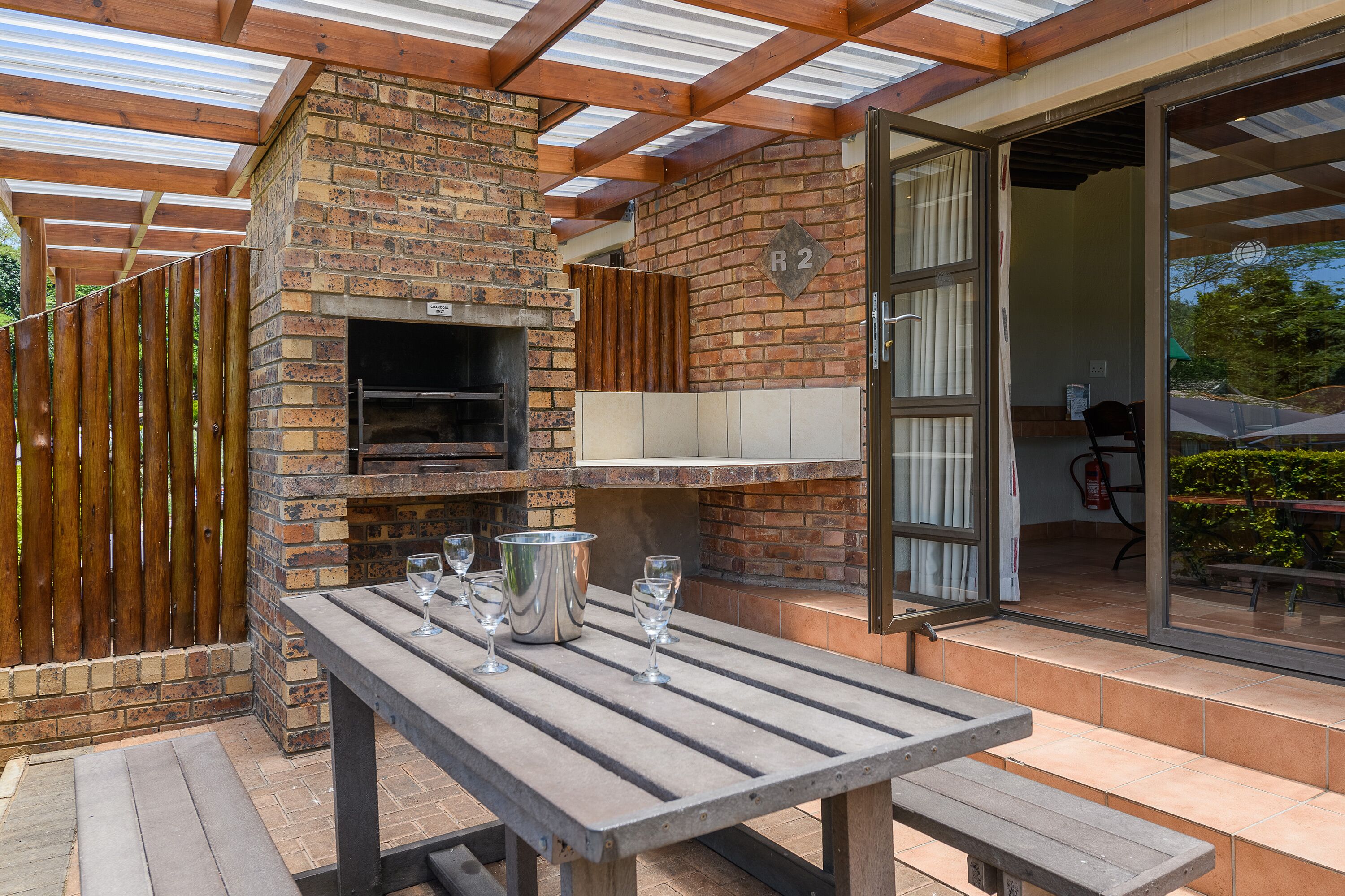 An outdoor patio with a brick oven, a table with glasses, and a wooden fence.