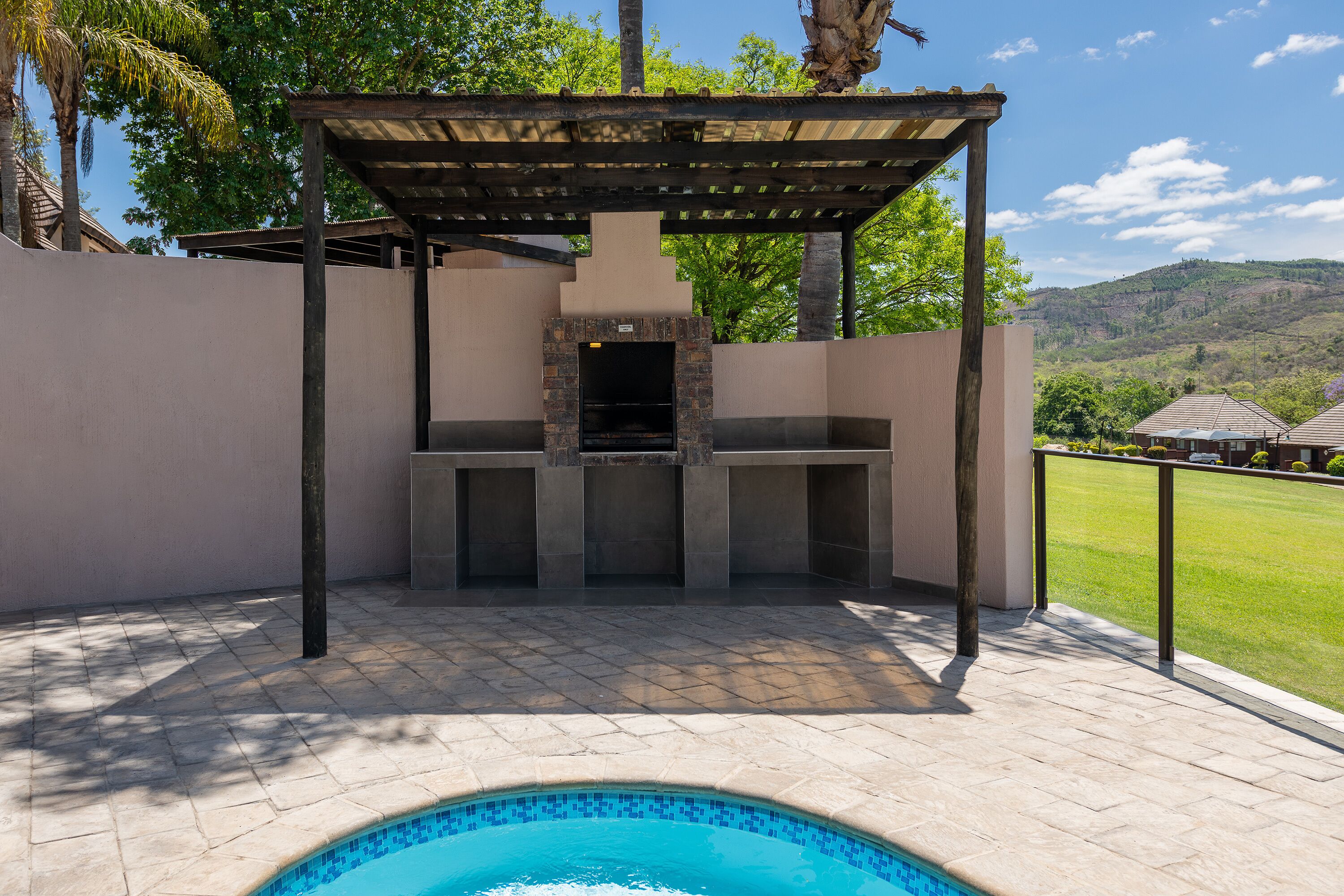 Un patio exterior con piscina de piedra, zona de barbacoa y vistas a un paisaje verde.