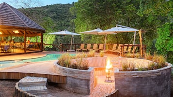 Zona junto a la piscina con terraza de madera, sillones de descanso y sombrillas.