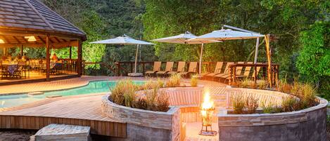 A poolside area with a wooden deck, lounge chairs, and umbrellas.