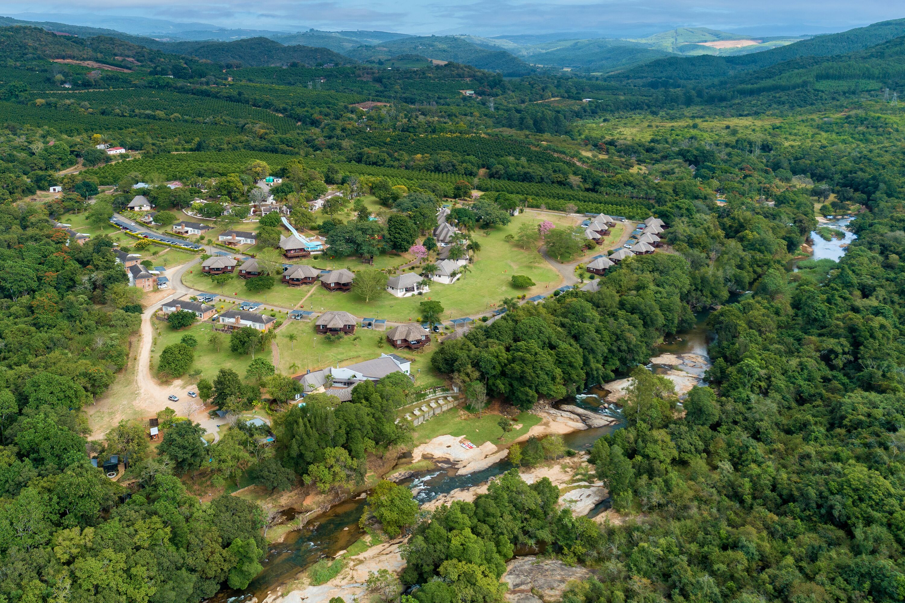 An aerial view of a rural area with a cluster of houses arranged in a semi-circular pattern around a central green space, with a river running through the middle.