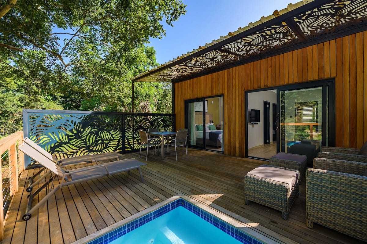 A wooden deck with a pool, wicker furniture, and a glass door leading to a room.