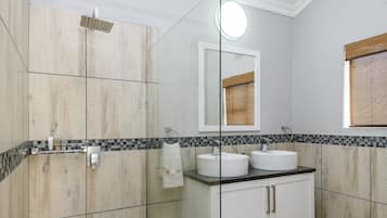 Un baño moderno con cabina de ducha de vidrio, tocador blanco con dos lavamanos y espejo sobre el tocador.