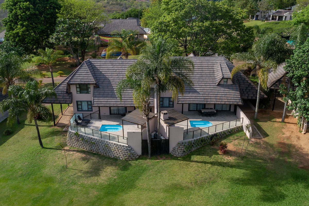 A two-story house with a swimming pool, surrounded by trees and a well-maintained lawn.