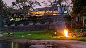 Vue sur un chalet au bord de la rivière, avec un espace extérieur aménagé et un feu de camp.