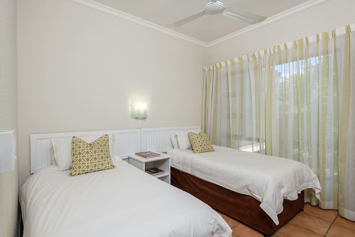 A hotel room with two beds, a nightstand, a ceiling fan, and a window with curtains.