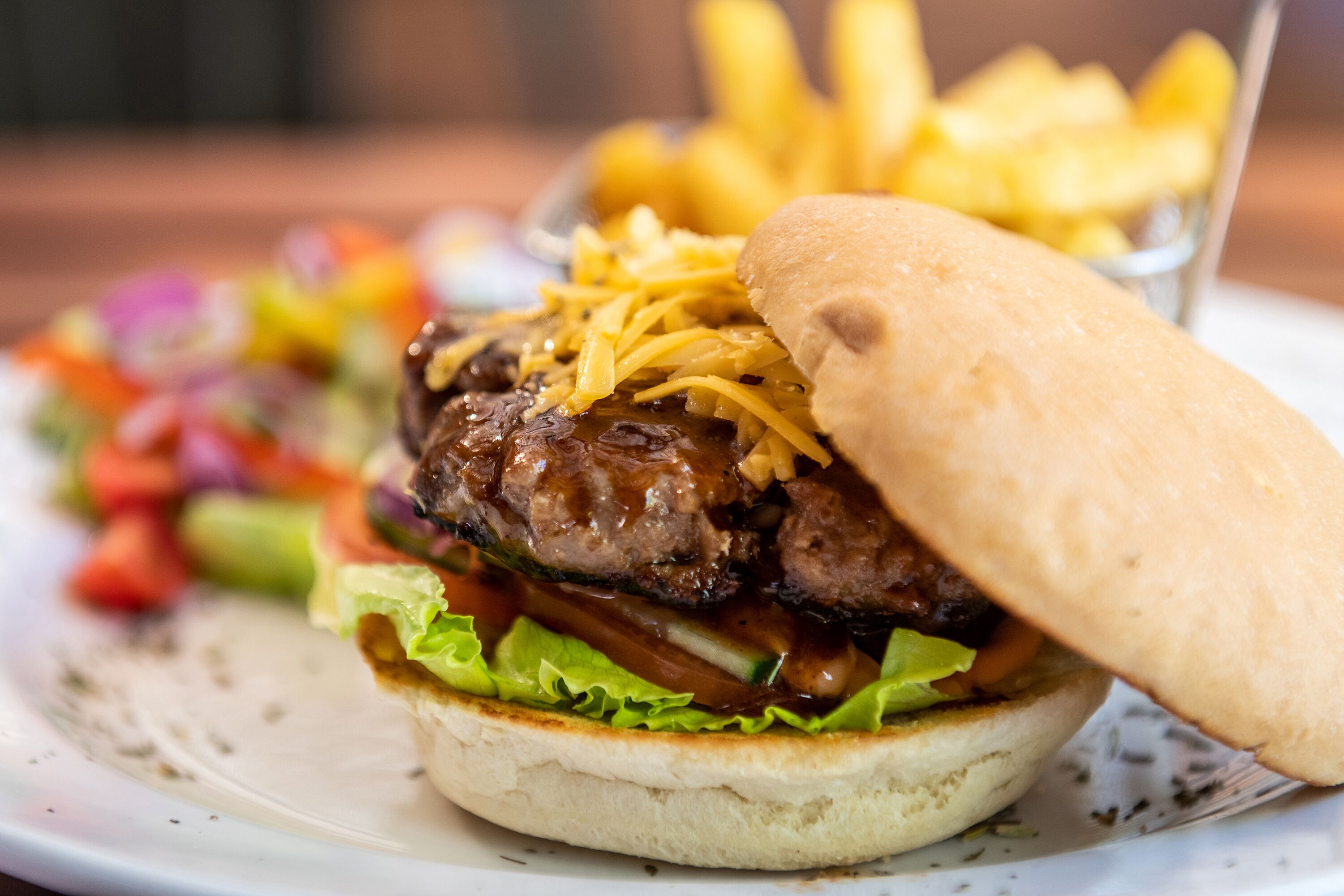 Een hamburger met kaas en sla op een broodje, geserveerd met friet en een salade.