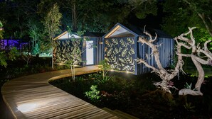 Un sentier en bois mène à un bâtiment dont les murs sont ornés de motifs de feuilles, le tout étant entouré d’une végétation luxuriante.