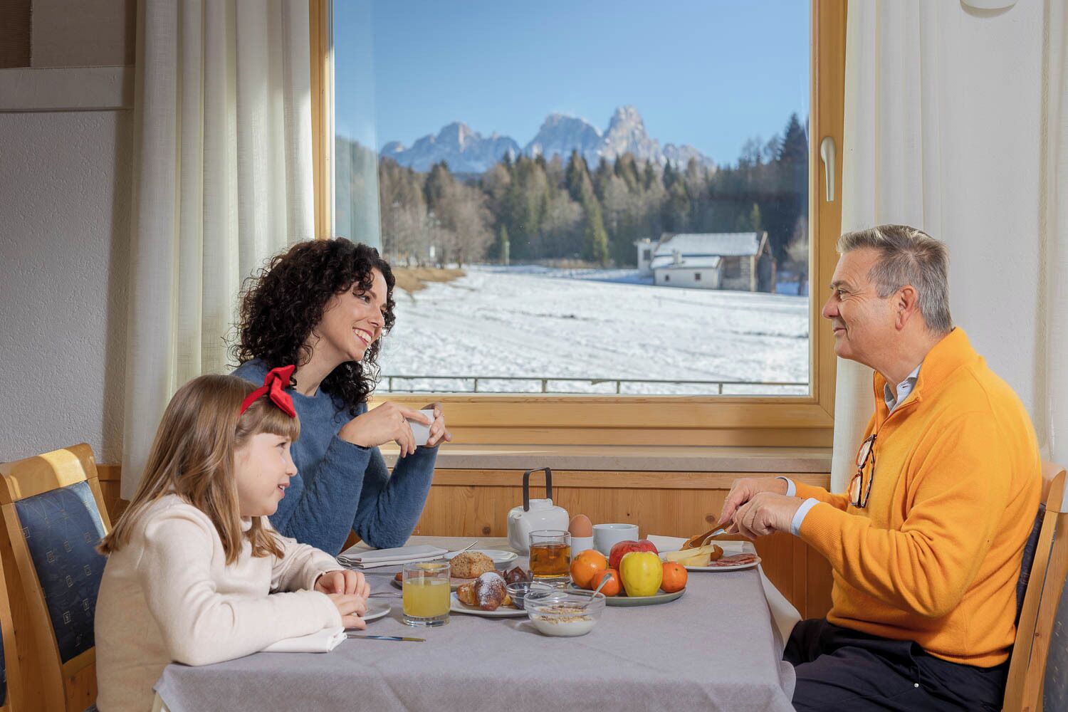 Una mesa de comedor con alimentos para el desayuno, una ventana que ofrece vistas a un paisaje nevado y un banco de madera.