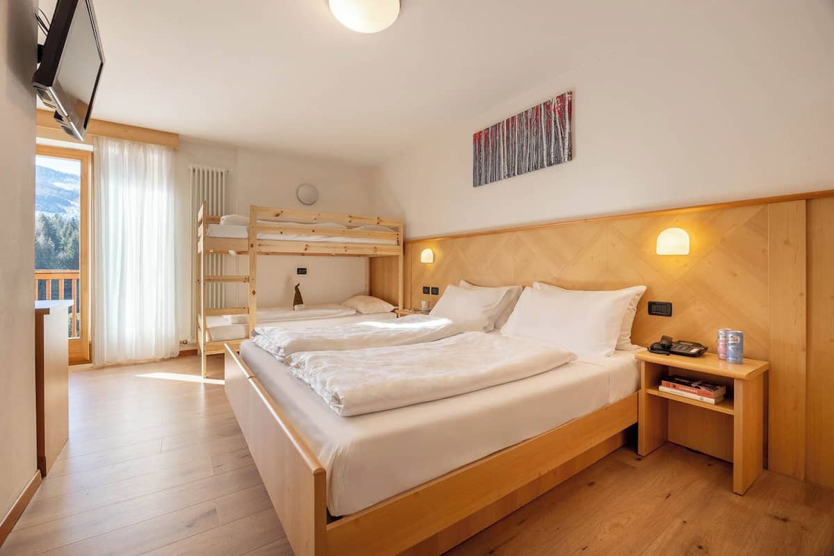 A room with two beds, a bunk bed, wooden flooring, a painting, and a nightstand with books and cans.