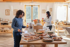 A breakfast buffet with various pastries, cakes, and a fruit basket.
