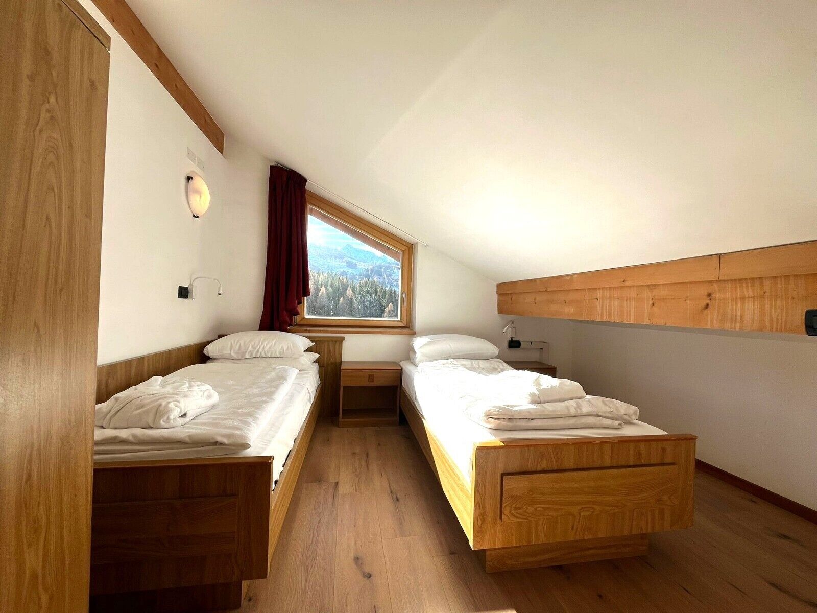 Una habitación pequeña y acogedora con dos camas de madera, una ventana que da a un bosque y un techo de madera.