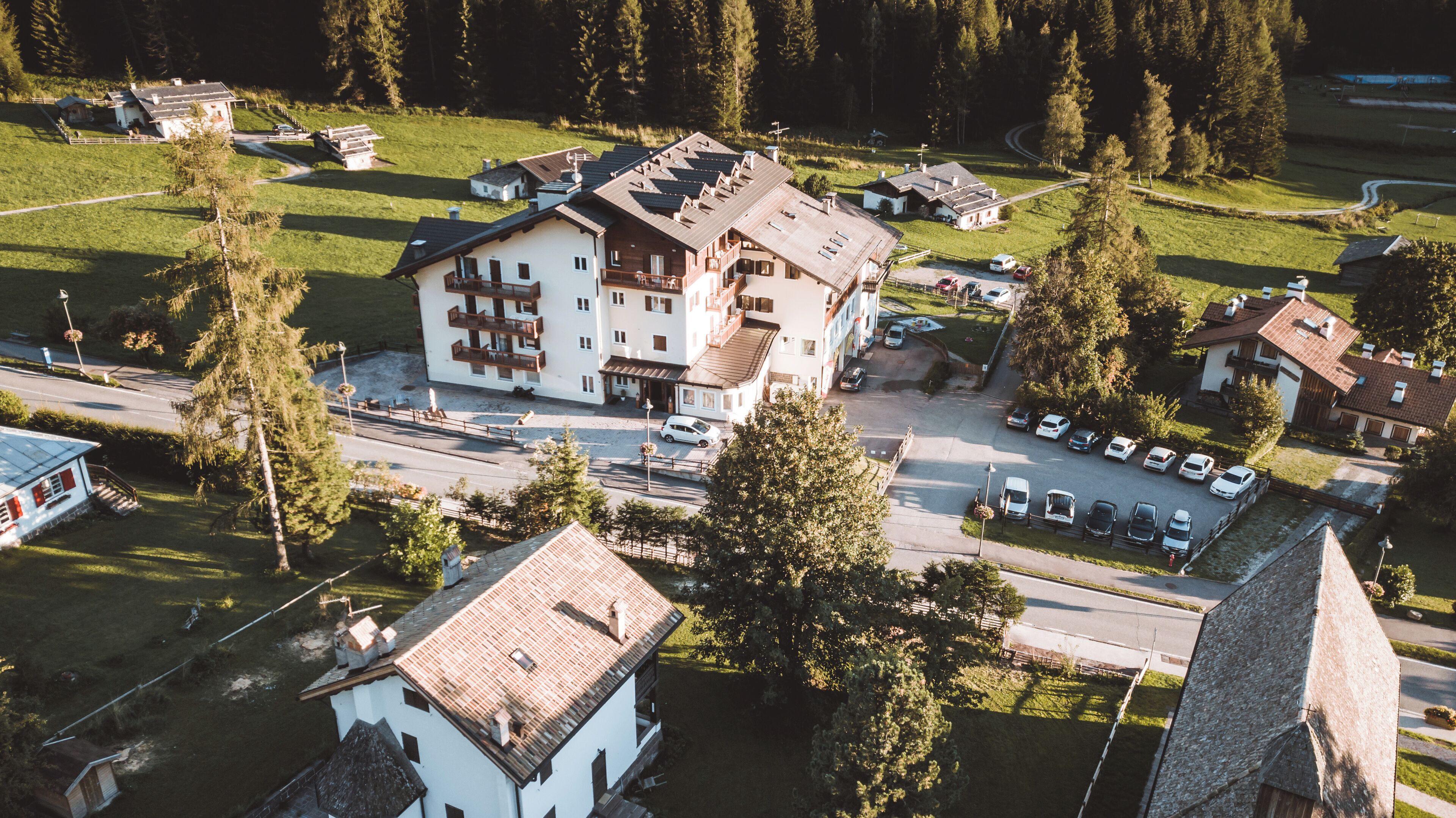 Un edificio a più piani con tetto spiovente, circondato da un parcheggio e aree verdi.