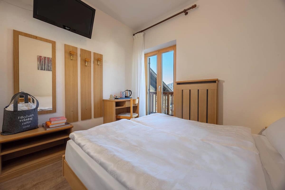 A hotel room with a bed, a desk, a chair, a TV, and a window with a view of the outside.