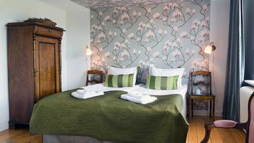 Ein ordentlich bezogenes Bett mit grüner Bettwäsche, zwei Nachttische mit Lampen, ein Holzschrank und Blumenpapier.