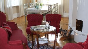 Una sala de estar con sillones rojos, una mesa de centro redonda de madera, un tapete estampado y una chimenea blanca.