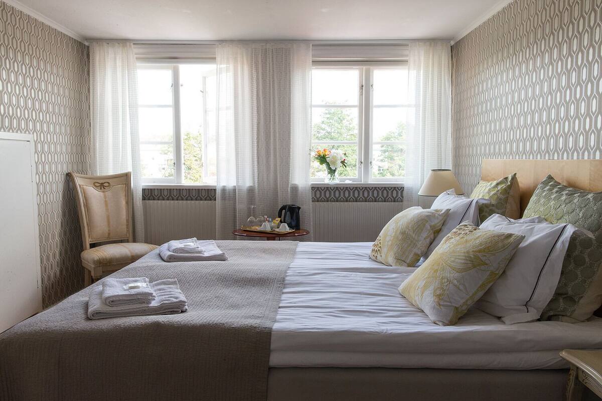A hotel room with a large bed, a chair, a table with a tray, and a window with curtains.