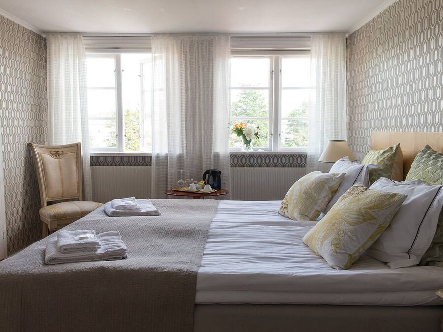Ett hotellrum med en stor säng, en stol, ett bord med ett bricka på och ett fönster med gardiner.