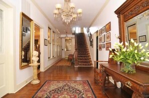 A grand hallway with a wooden staircase, a chandelier, and framed artwork on the walls.