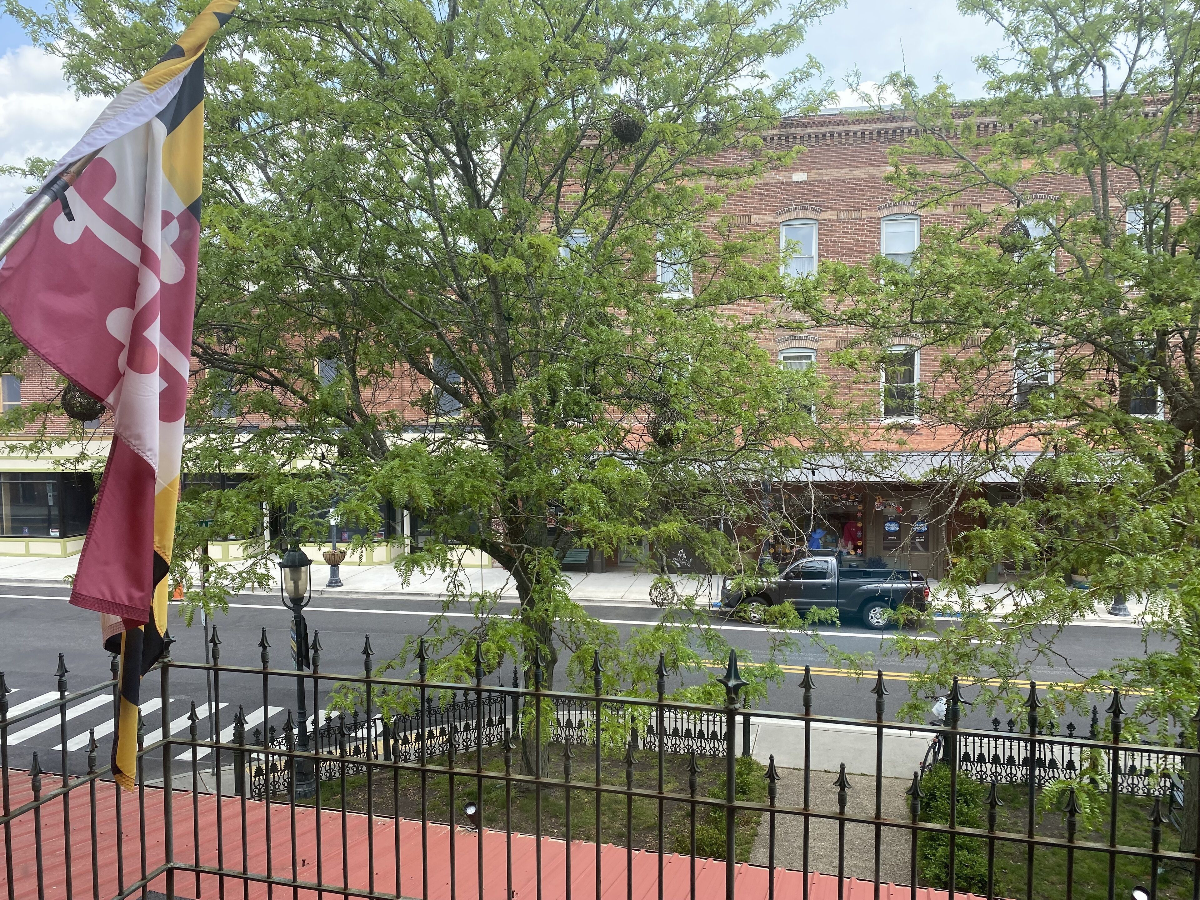A flagpole with a flag, a tree, and a brick building in the background.