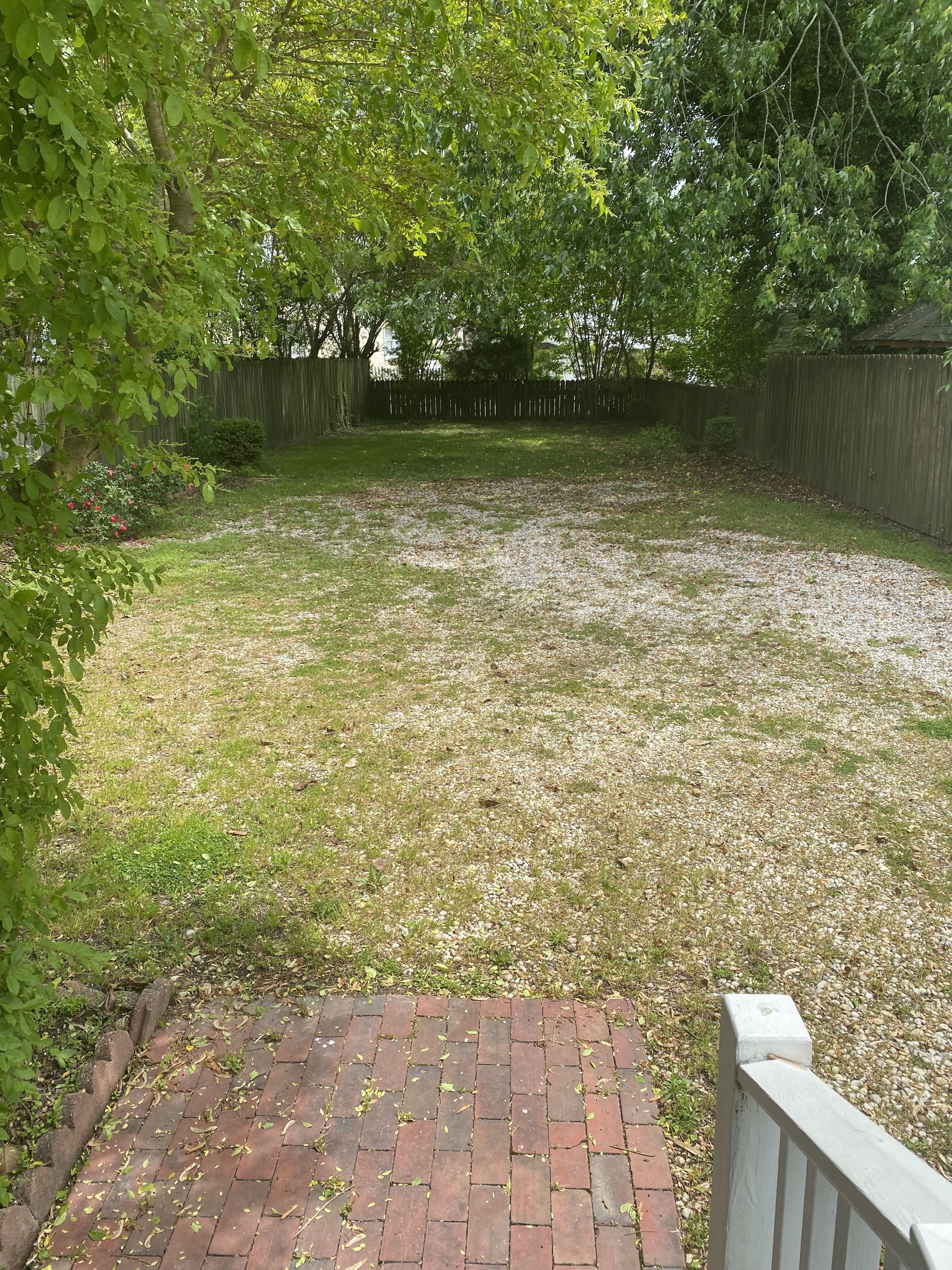 Een achtertuin met een met bakstenen bestraat pad dat leidt naar een houten terras.