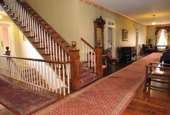 A staircase with a wooden handrail and white balusters, leading to a landing with a red patterned rug.