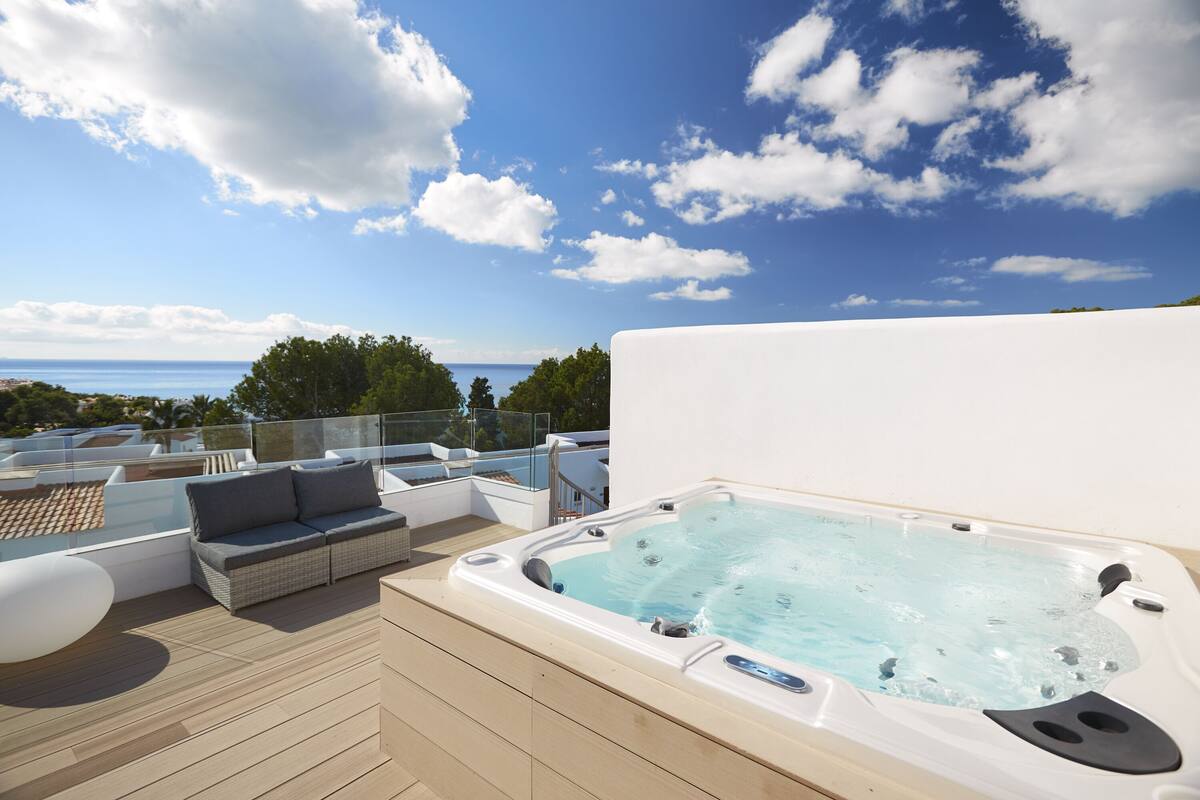 A rooftop deck with a hot tub, outdoor furniture, and a view of the sea.
