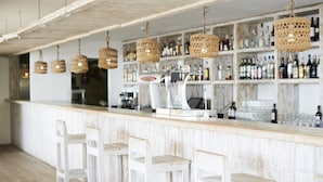 A bar area with white bar stools, wicker hanging lights, and shelves stocked with bottles. - Insotel Tarida Beach Resort & SPA - All inclusive (Sant Josep de sa Talaia)