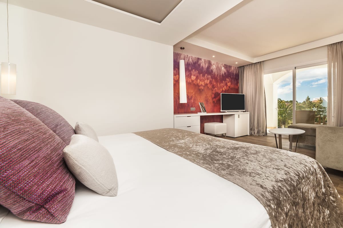 A modern hotel room with a large bed, a desk, a TV, and a sofa.