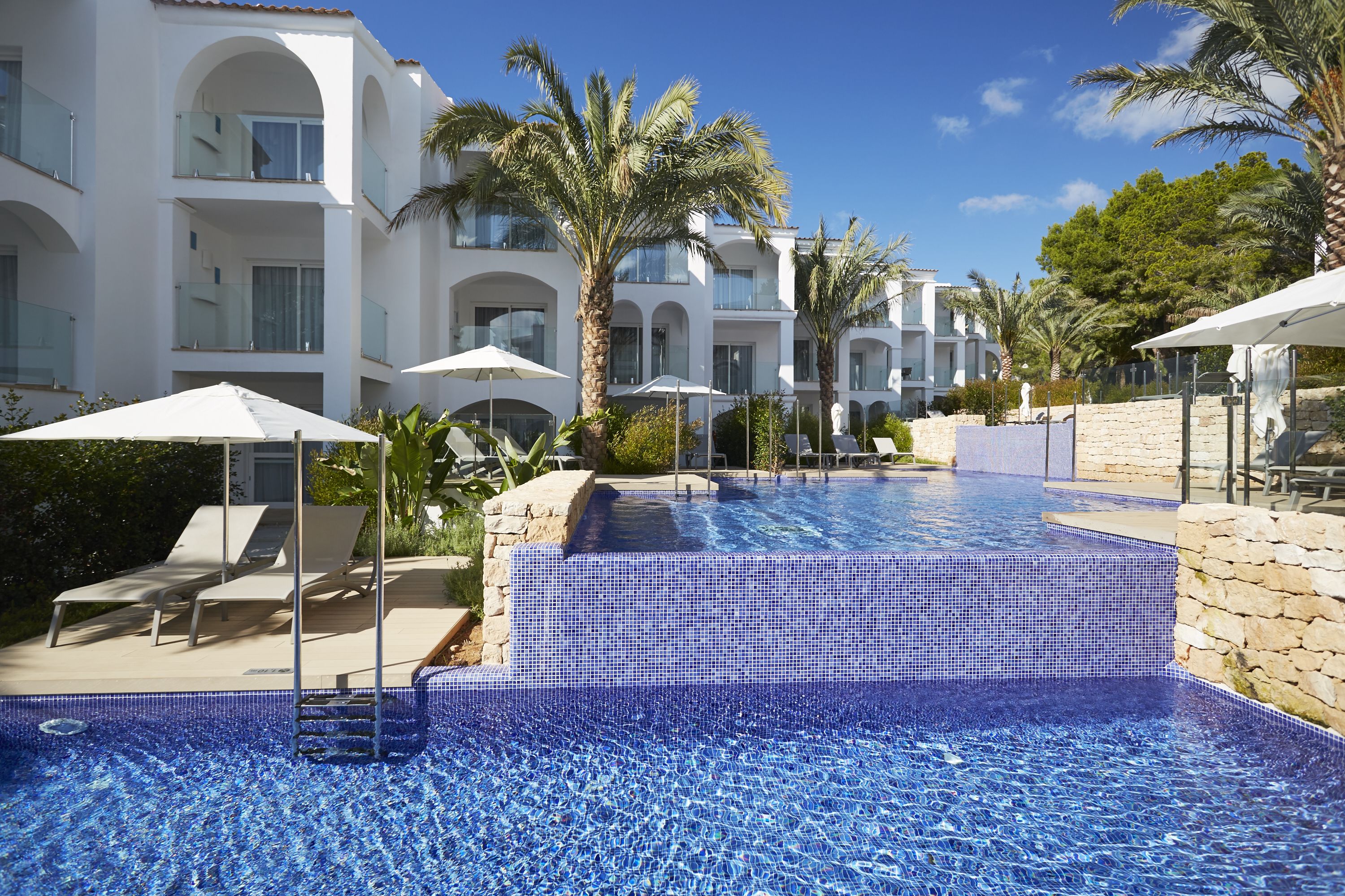 A pool area with tiled steps, lounge chairs, and umbrellas.